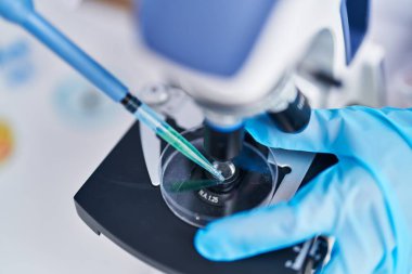 Young woman scientist pouring liquid on sample using microscope at laboratory