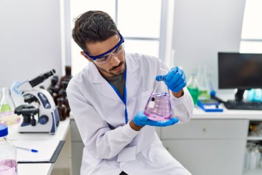 Laboratuvarda deney tüpü tutan bilim adamı üniforması giyen İspanyol genç adam.