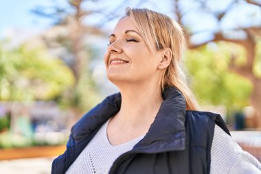 Parkta gözleri kapalı nefes alan genç sarışın kadın.