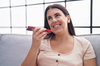 Evdeki kanepede oturmuş akıllı telefondan konuşan genç, güzel İspanyol kadın.
