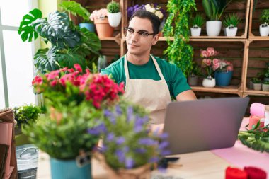 Young hispanic man florist smiling confident using laptop at flower shop