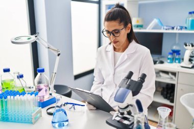 Laboratuvarda çalışan, bilim adamı üniforması giyen genç İspanyol kadın.