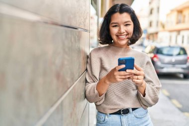 Sokakta akıllı telefon kullanan kendine güvenen genç bir kadın.