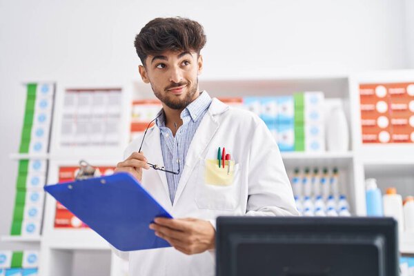 Young arab man pharmacist smiling confident reading document at pharmacy