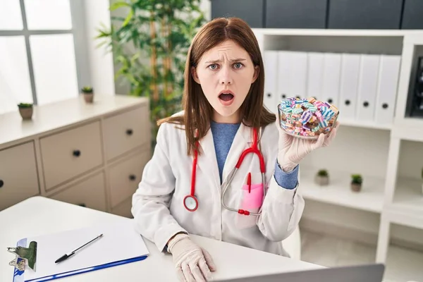 Young Doctor Woman Holding Sweets Candy Scared Amazed Open Mouth — Stock Photo, Image