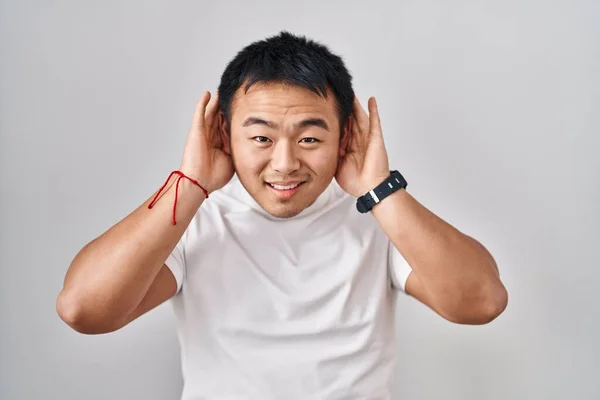 若い中国人男性の白い背景の上に耳のジェスチャーで両方の手を聞いて ゴシップを好奇心をしようと立っている 聴覚障害や聴覚障害 — ストック写真