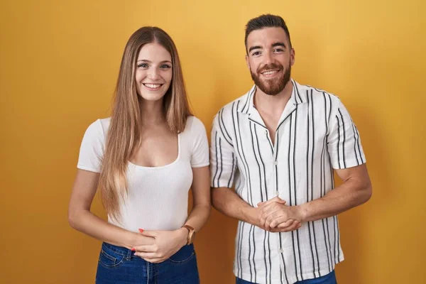 Sarı Arka Planda Duran Genç Çift Ellerini Kavuşturup Gülümseyerek Gevşemiş — Stok fotoğraf