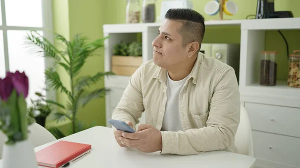 Junger Hispanischer Mann Sitzt Mit Smartphone Auf Tisch Esszimmer — Stockfoto