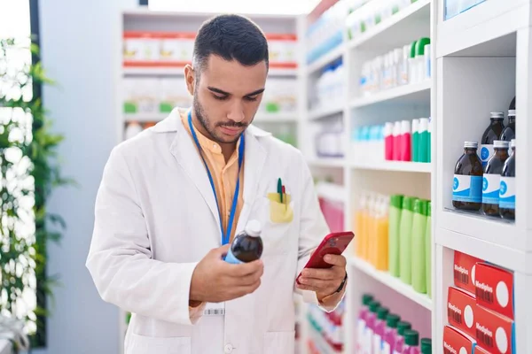 Young Hispanic Man Pharmacist Using Smartphone Holding Medication Bottle Pharmacy — Foto Stock