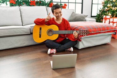 Kısa saçlı İspanyol bir kadın, internetten klasik gitar öğreniyor. Bir fikir ya da soru işareti ile şaşırdı. 
