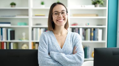 Young beautiful hispanic woman student smiling confident standing with arms crossed gesture at library university