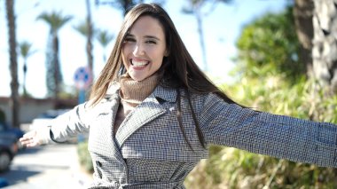 Güzel İspanyol kadın gülümsüyor. Parkta kolları açık duruyor.