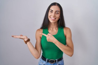 Young woman standing over isolated background amazed and smiling to the camera while presenting with hand and pointing with finger. 