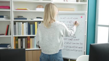 Young blonde woman teaching maths on magnetic board at library university