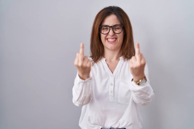 Brunette woman standing over white isolated background showing middle finger doing fuck you bad expression, provocation and rude attitude. screaming excited 
