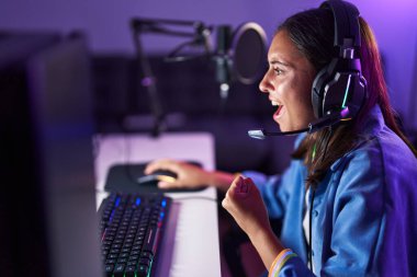 Genç, İspanyol asıllı, güzel bir kadın oyuncu oyun odasında video oyunu oynuyor.