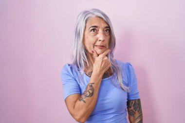 Pembe arka planda duran orta yaşlı bir kadın bir soru hakkında endişeli ve gergin bir şekilde düşünüyor. 