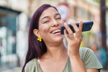 Genç, güzel, İspanyol bir kadın gülümsüyor ve caddede akıllı telefondan konuşuyor.
