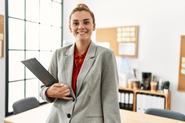 Ofiste elinde pano tutarak gülümseyen genç bir iş kadını.