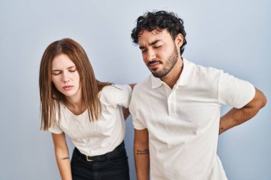 Genç çift gündelik giysiler giyip sırt ağrısından muzdarip olarak yan yana duruyorlar. Elleriyle dokunuyorlar, kasları ağrıyor. 