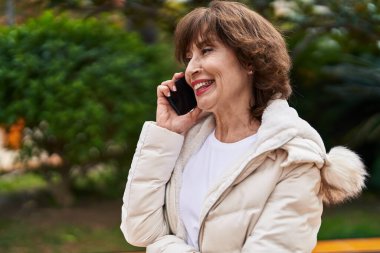 Orta yaşlı bir kadın gülümsüyor. Parktaki akıllı telefondan konuşuyor.