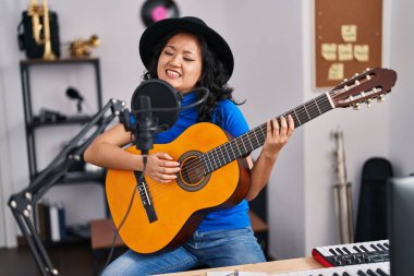 Genç Çinli kadın sanatçı müzik stüdyosunda gitar çalarak şarkı söylüyor.