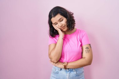 Pembe arka planda duran genç İspanyol kadın çapraz kollu depresyon sorunlarından yorgun ve sıkılmış göründüğünü düşünüyor.. 