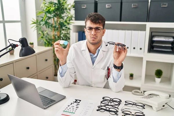 Young Hispanic Oculist Holding Glasses Contact Lenses Skeptic Nervous Frowning — Stock Photo, Image