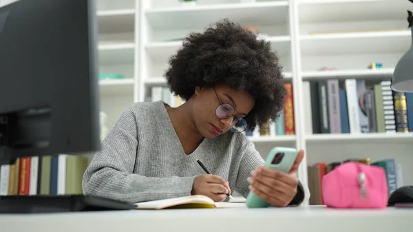 African American Woman Student Using Smartphone Writing Notebook Library University — Stockfoto