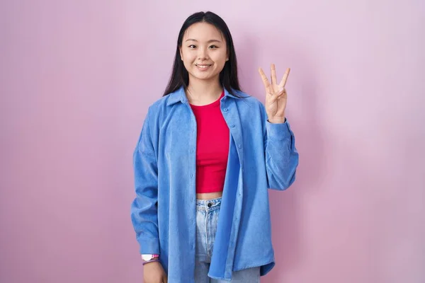 Молодая Азиатка Стоящая Розовом Фоне Показывающая Пальцами Номер Три Улыбаясь — стоковое фото