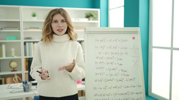 Young blonde woman teacher explaining maths exercise at university classroom