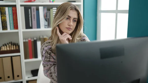 在图书馆大学里 年轻的金发女学生正在用计算机学习 其表情令人生疑 — 图库照片