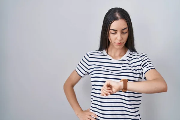 年轻的黑发女人穿着条纹T恤检查腕表上的时间 放松而自信 — 图库照片