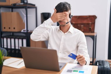 Bilgisayarla çalışan İspanyol genç adam elinde kredi kartıyla gözlerini kapatıyor, ciddi ve üzgün görünüyor. Görme, saklama ve reddetme konsepti 