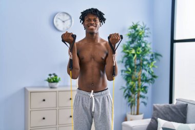 African american man smiling confident training arms exercise using elastic band at home