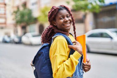 African american woman student smiling confident holding books at street