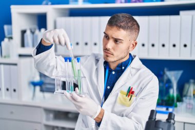 Young hispanic man scientist holding test tubes at laboratory