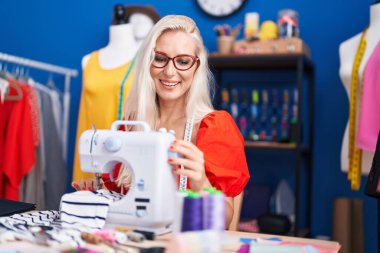 Dikiş atölyesinde dikiş makinesi kullanan kendine güvenen genç sarışın kadın terzi.