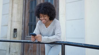 Afro-Amerikalı kadın sokakta akıllı telefon kullanarak kendine güveniyor.