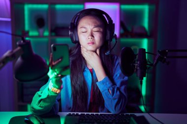 Genç Asyalı bir kadın video oyunları oynuyor. Akıllı telefonuyla boynuna dokunuyor. Grip, mantar ve enfeksiyon yüzünden boğaz ağrısı çekiyor. 
