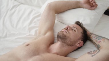 Young caucasian man lying on bed sleeping shirtless at bedroom
