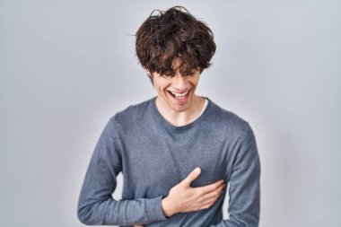 İzole edilmiş arka planda duran genç adam gülümseyerek ve kahkahalarla gülüyor çünkü elleri vücutta olan komik çılgın bir şaka.. 