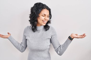 Koyu renk saçlı İspanyol kadın izole edilmiş arka planda gülümseyerek avuçlarını açıyor, sunuyor, reklamını yapıyor, karşılaştırıyor ve dengede duruyor. 