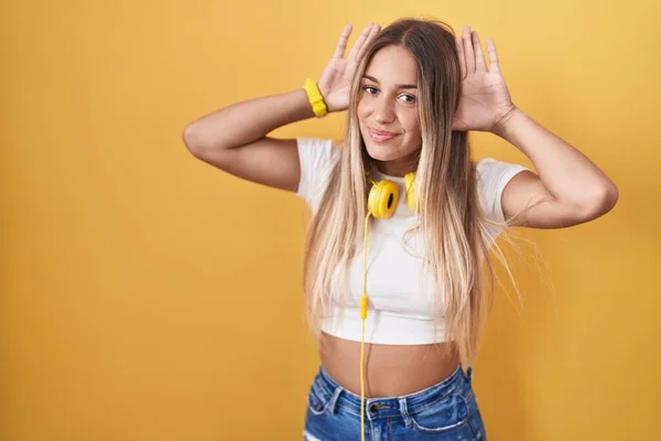 Młoda Blondynka Stojąca Nad Żółtym Tłem Nosząca Słuchawki Próbująca Usłyszeć — Zdjęcie stockowe
