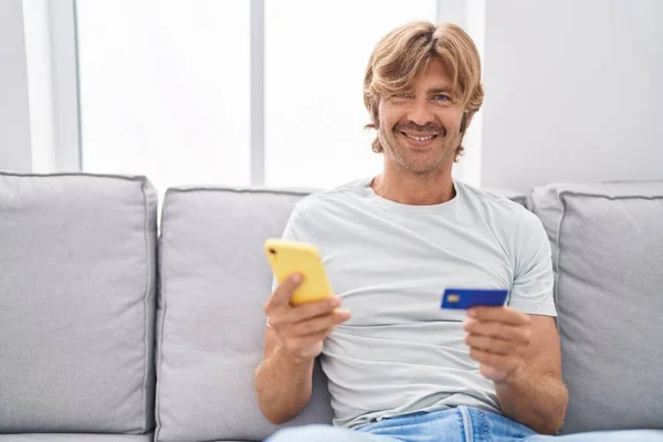 Jovem Usando Smartphone Cartão Crédito Sentado Sofá Casa — Fotografia de Stock