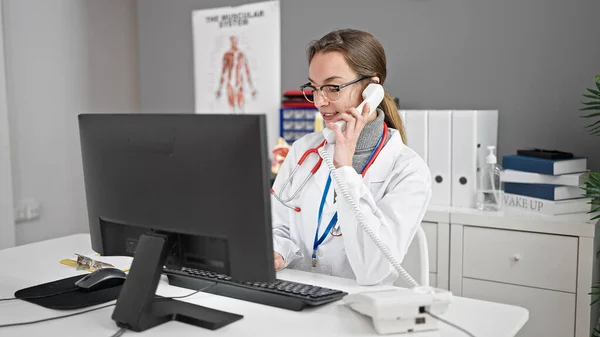 年轻的高加索女医生在诊所用计算机通过电话交谈 — 图库照片