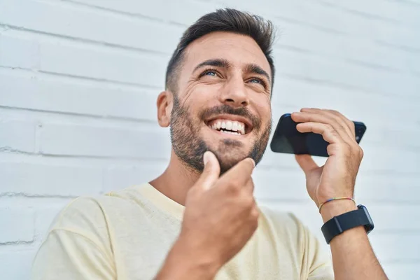 Молодий Іспаномовний Чоловік Посміхається Впевнено Слухаючи Аудіоповідомлення Смартфону Над Ізольованим — стокове фото