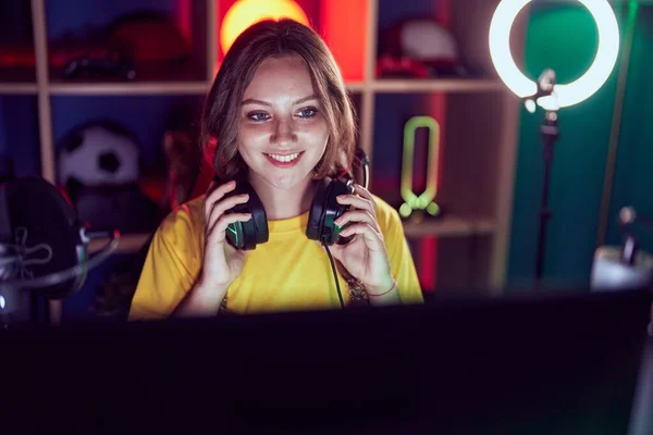 年轻的金发女子带着自信的笑容在游戏室拿着耳机 — 图库照片