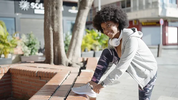 stock image African american woman wearing headphones tying shoe at park