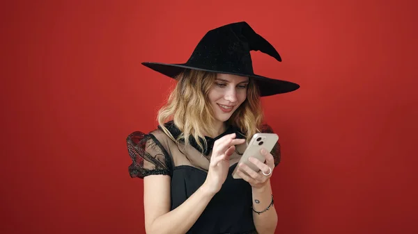 Jovem Loira Vestindo Traje Bruxa Usando Smartphone Sobre Fundo Vermelho — Fotografia de Stock